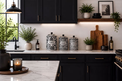 a modern kitchen with black cabinets, white countertops, and various decorative elements such as potted plants, vases, and a wooden cutting board.